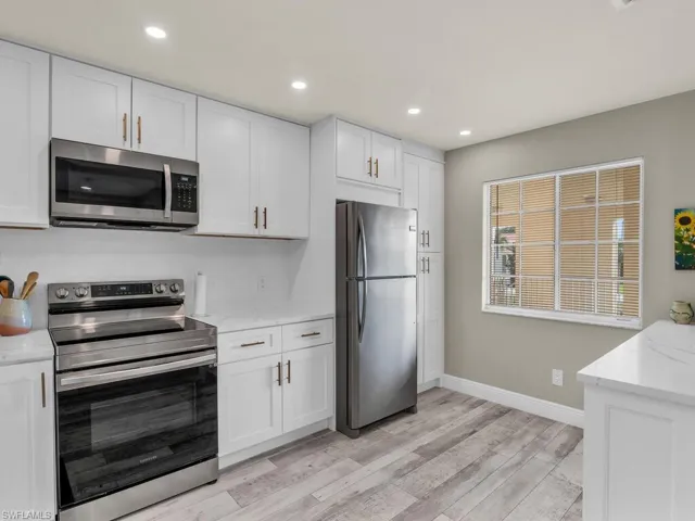 Kitchen with appliances with stainless steel finishes, light stone counters, white cabinetry, and light hardwood / wood-style flooring