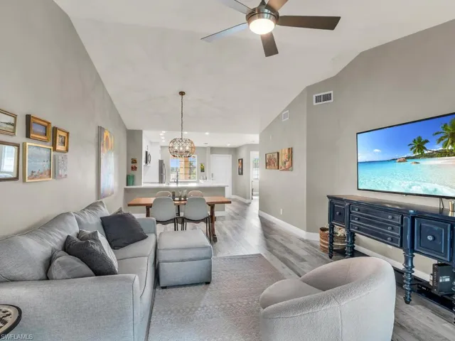 Living room featuring light hardwood / wood-style flooring, ceiling fan with notable chandelier, and high vaulted ceiling