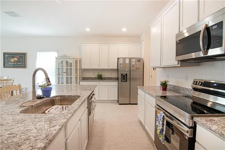 Kitchen with appliances with stainless steel finishes, white cabinetry, light stone counters, and recessed lighting