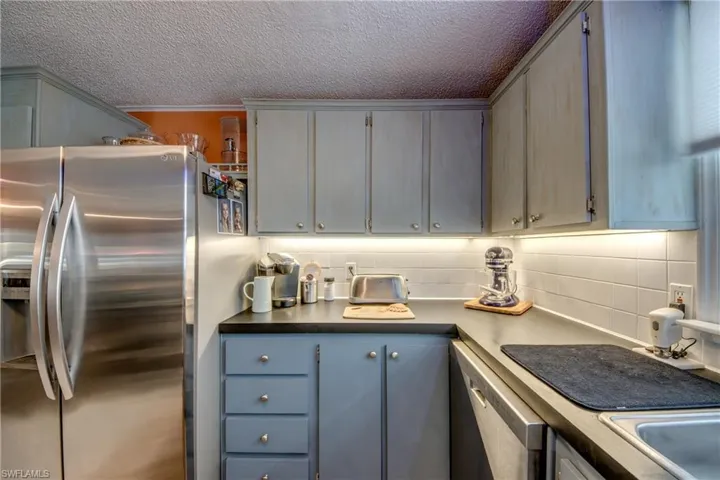 Kitchen featuring gray cabinets, appliances with stainless steel finishes, a textured ceiling, and backsplash