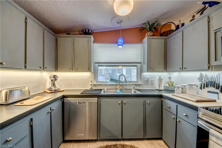 Kitchen with gray cabinetry, stainless steel dishwasher, and hanging light fixtures