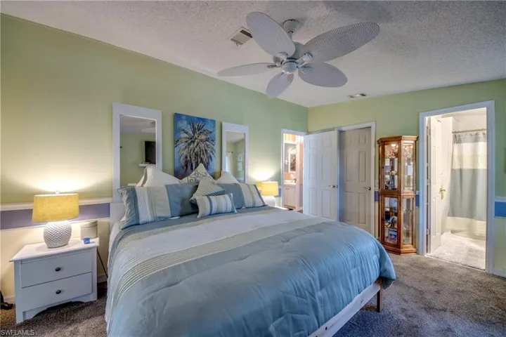 Carpeted bedroom featuring ceiling fan, ensuite bath, a textured ceiling, and vaulted ceiling