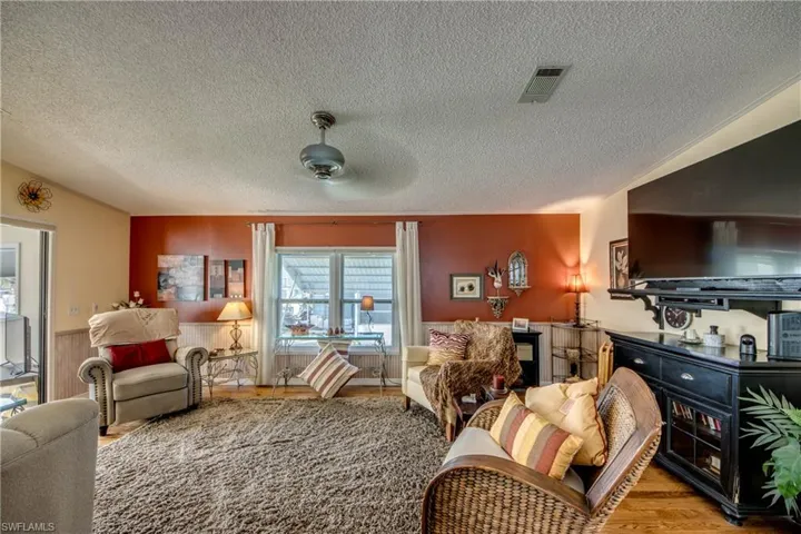 Living room with ceiling fan, a textured ceiling, and light hardwood / wood-style floors