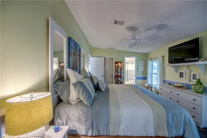 Bedroom with a closet, connected bathroom, a textured ceiling, vaulted ceiling, and ceiling fan