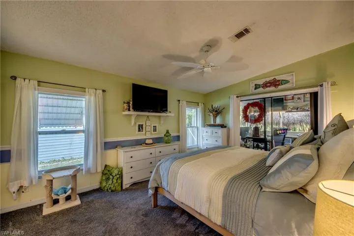 Carpeted bedroom featuring a textured ceiling, lofted ceiling, multiple windows, and ceiling fan