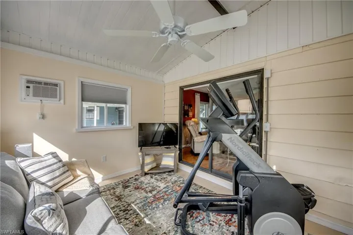 Exercise room featuring wood walls, ceiling fan, vaulted ceiling, and a wall mounted air conditioner