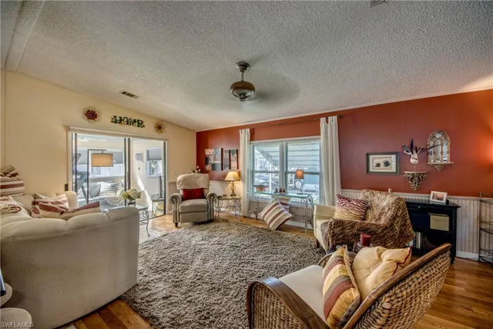Living room featuring hardwood / wood-style floors, ceiling fan, a textured ceiling, and vaulted ceiling
