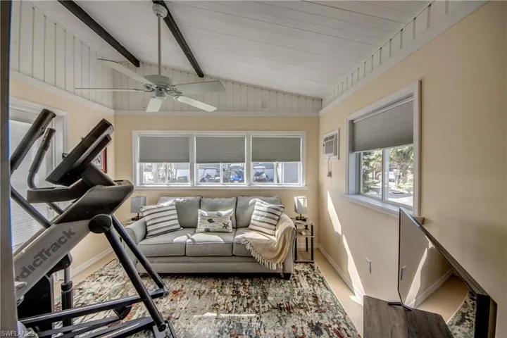 Exercise room with an AC wall unit, lofted ceiling, and ceiling fan