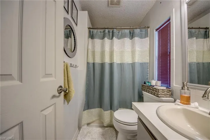 Bathroom with toilet, a shower with curtain, vanity, and a textured ceiling