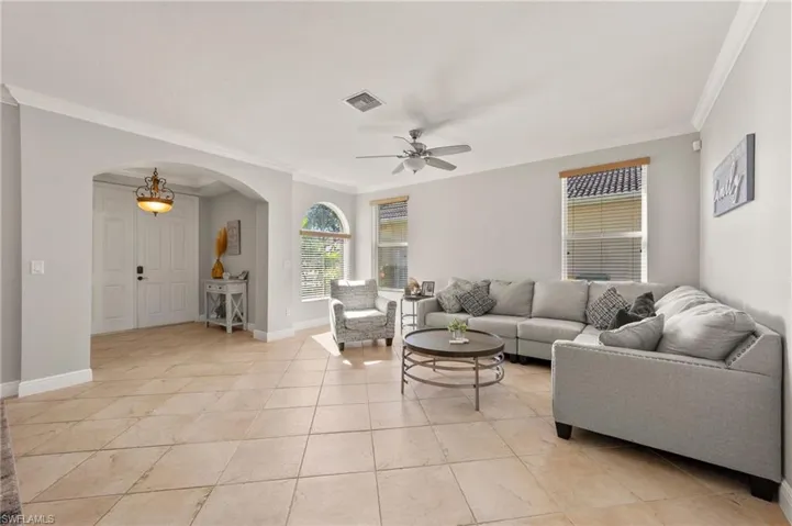 Living room featuring ceiling fan, light tile patterned floors, and crown molding