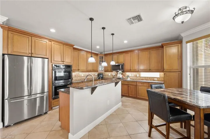 Kitchen with appliances with stainless steel finishes, ornamental molding, dark stone counters, pendant lighting, and an island with sink