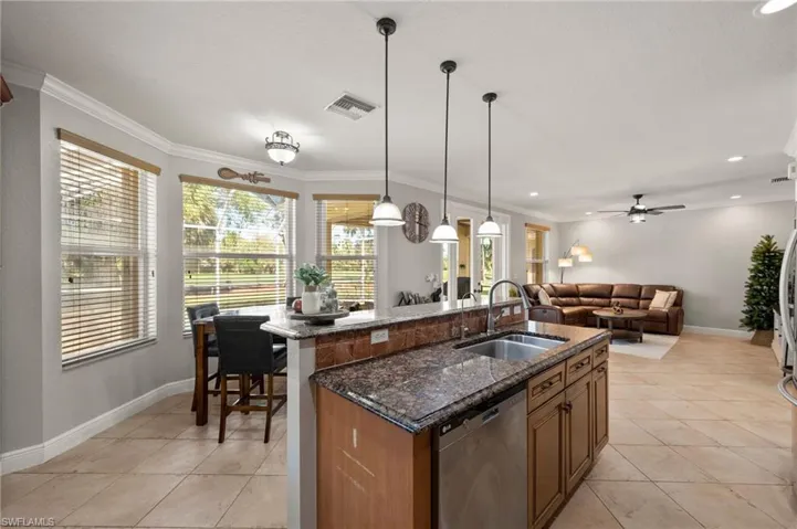 Kitchen with a kitchen island with sink, sink, dark stone countertops, dishwasher, and hanging light fixtures