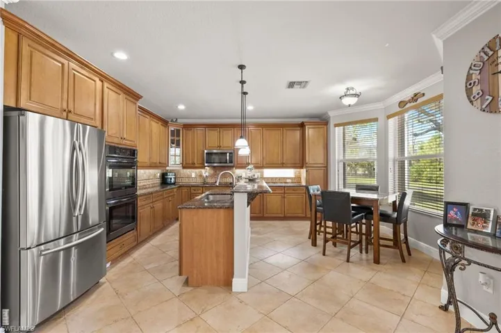 Kitchen featuring stainless steel appliances, crown molding, dark stone counters, decorative light fixtures, and a kitchen island with sink