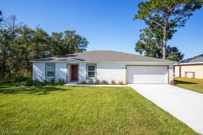 Ranch-style house featuring a front lawn, an attached garage, stucco siding, and concrete driveway