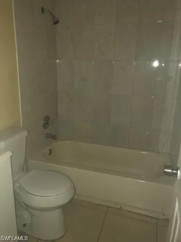 Bathroom featuring tiled shower / bath, tile flooring, and toilet