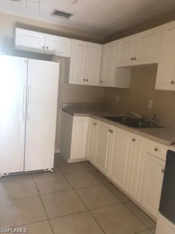 Kitchen featuring white cabinets, sink, white fridge, and light tile floors
