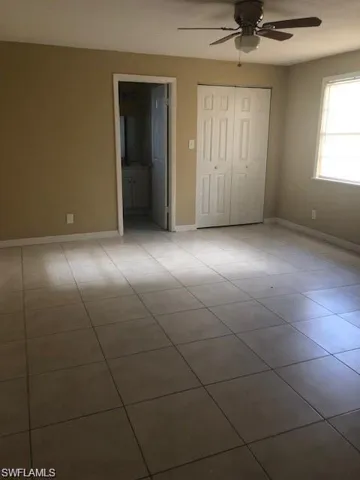 Unfurnished bedroom featuring a closet, light tile flooring, ceiling fan, and ensuite bath