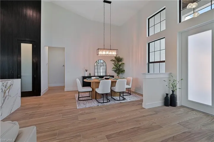 Vaulted ceilings, wood-finish flooring, tall windows, a prominent black accent wall, and a marble-clad half-wall