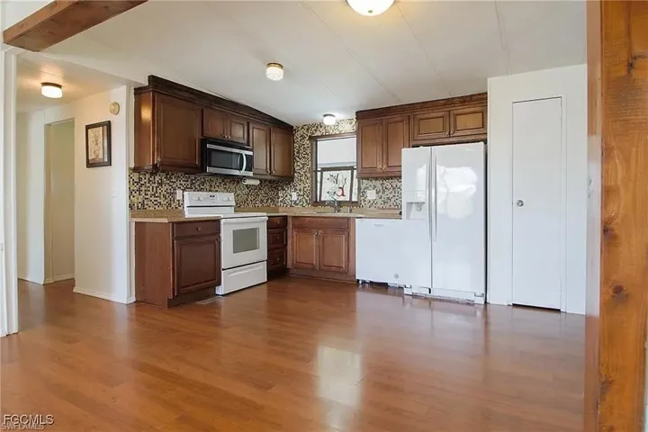 Kitchen featuring white appliances, light countertops, decorative backsplash, dark wood-style floors, and brown cabinets