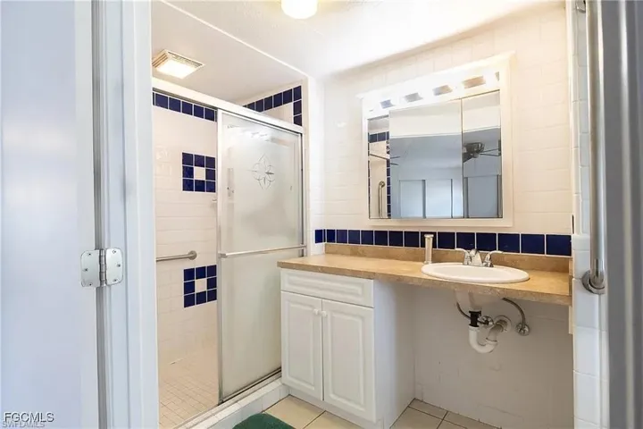 Bathroom with a shower stall, tasteful backsplash, light tile patterned flooring, tile walls, and vanity