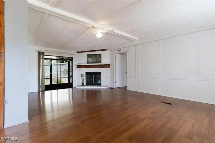 Unfurnished living room with a ceiling fan, a decorative wall, a glass covered fireplace, and dark wood-type flooring