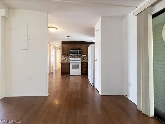 Kitchen with dark brown cabinets, dark wood-style flooring, white appliances, and backsplash