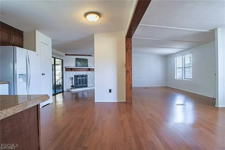 Unfurnished living room with a stone fireplace and dark wood-style floors