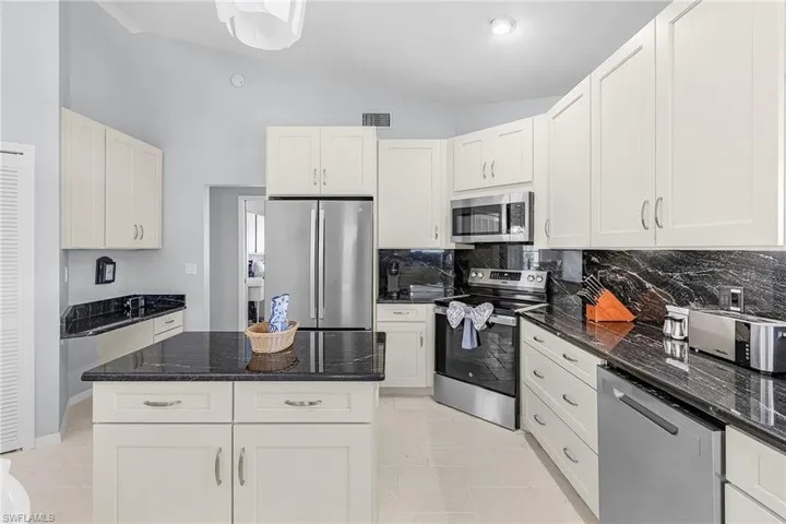Kitchen with vaulted ceiling, appliances with stainless steel finishes, dark stone countertops, a kitchen island, and tasteful backsplash