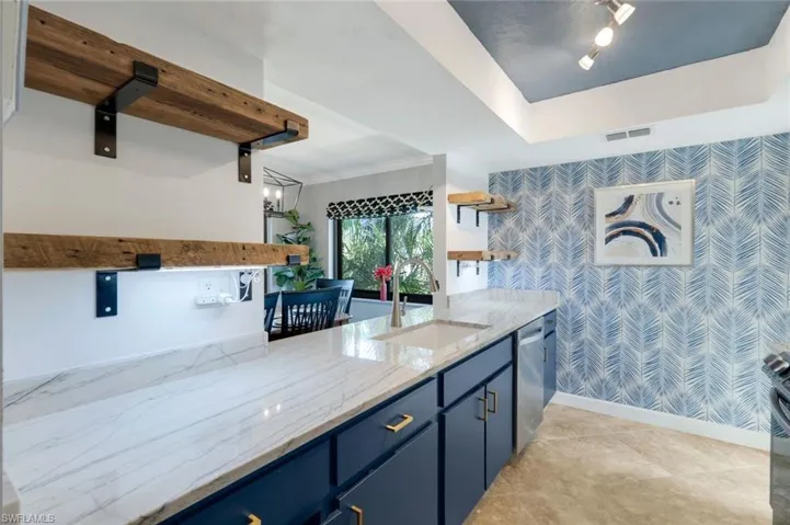Kitchen with light stone counters, stainless steel dishwasher, crown molding, sink, and blue cabinetry