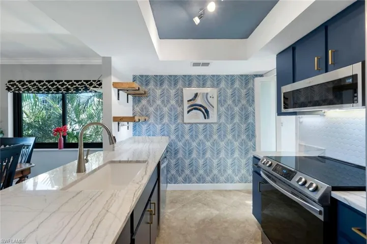 Kitchen featuring stainless steel appliances, a tray ceiling, crown molding, sink, and blue cabinetry