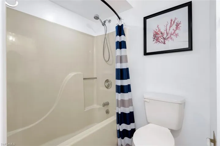 Bathroom featuring toilet and shower / bathtub combination with curtain