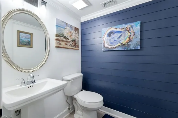 Bathroom featuring wood walls, toilet, ornamental molding, and sink