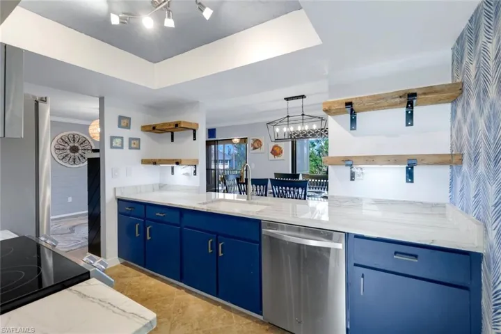Kitchen with sink, light stone counters, blue cabinets, appliances with stainless steel finishes, and ornamental molding