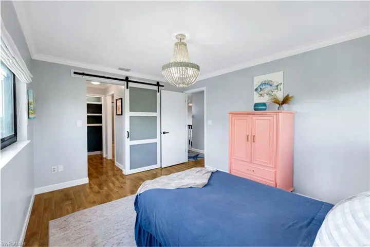 Bedroom featuring a walk in closet, ornamental molding, a barn door, a notable chandelier, and hardwood / wood-style floors