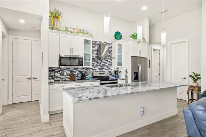 Kitchen with appliances with stainless steel finishes, wall chimney range hood, backsplash, light wood-style flooring, and white cabinets