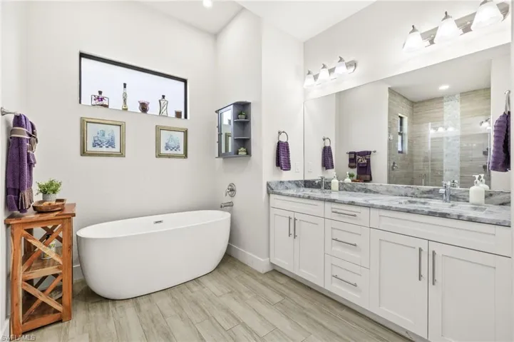 Full bathroom featuring double vanity, a stall shower, a freestanding tub, wood finished floors, and recessed lighting