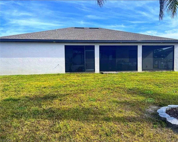 Back of property with a shingled roof, a yard, stucco siding, and a sunroom