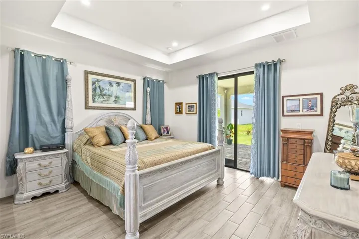 Bedroom featuring a tray ceiling, access to exterior, light wood finished floors, and recessed lighting