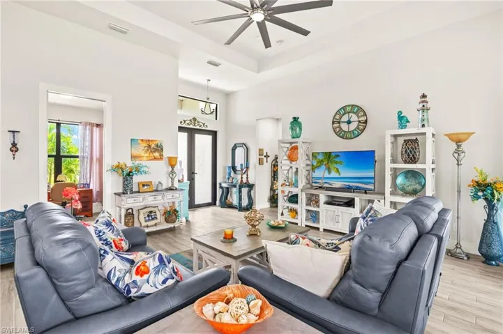 Living room featuring a ceiling fan, plenty of natural light, wood finished floors, a raised ceiling, and a high ceiling