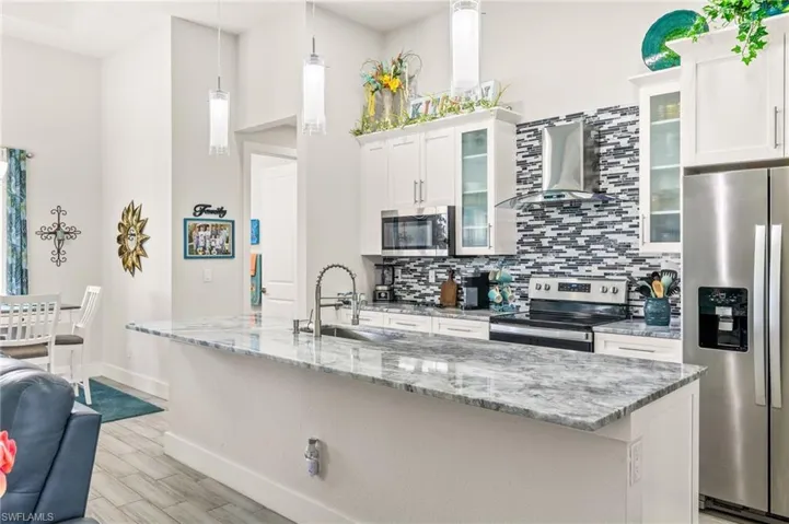 Kitchen featuring appliances with stainless steel finishes, wall chimney range hood, decorative backsplash, light wood-style flooring, and white cabinetry