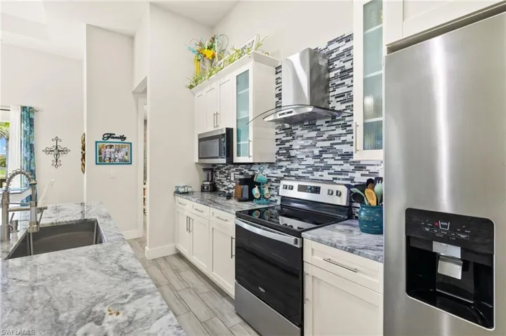 Kitchen featuring appliances with stainless steel finishes, wall chimney range hood, backsplash, and white cabinets