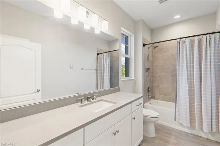 Bathroom with vanity, shower / bathtub combination with curtain, wood finished floors, and recessed lighting