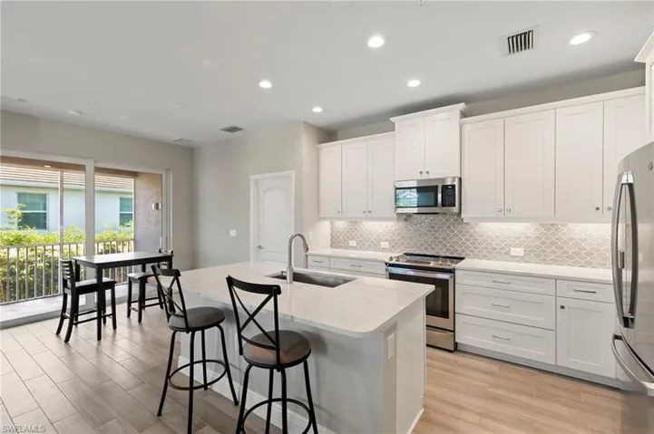 Kitchen featuring stainless steel appliances, tasteful backsplash, a center island with sink, light wood finished floors, and recessed lighting