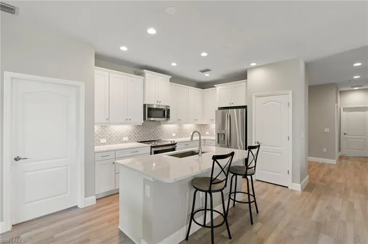 Kitchen featuring appliances with stainless steel finishes, backsplash, a breakfast bar, white cabinets, and light wood-type flooring