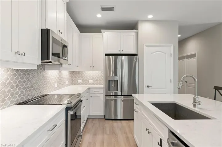 Kitchen featuring stainless steel appliances, light wood finished floors, white cabinetry, light stone countertops, and decorative backsplash