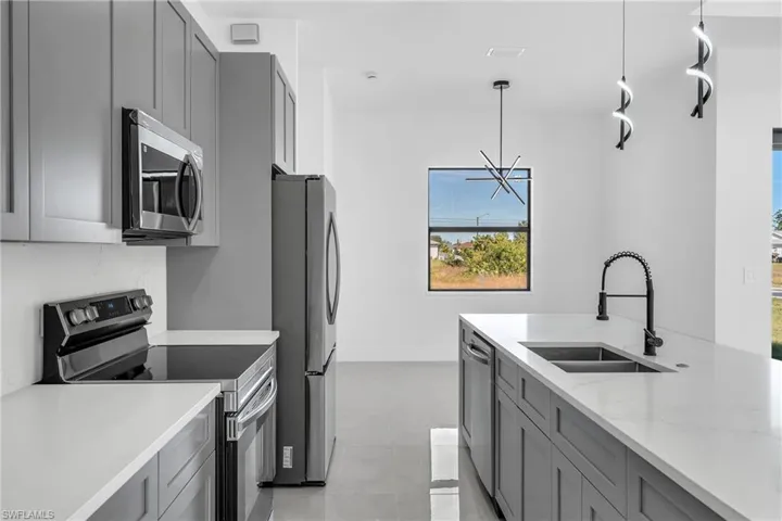 Dual tone kitchen with stainless steel appliances, light stone countertops, hanging light fixtures, and two tone cabinets