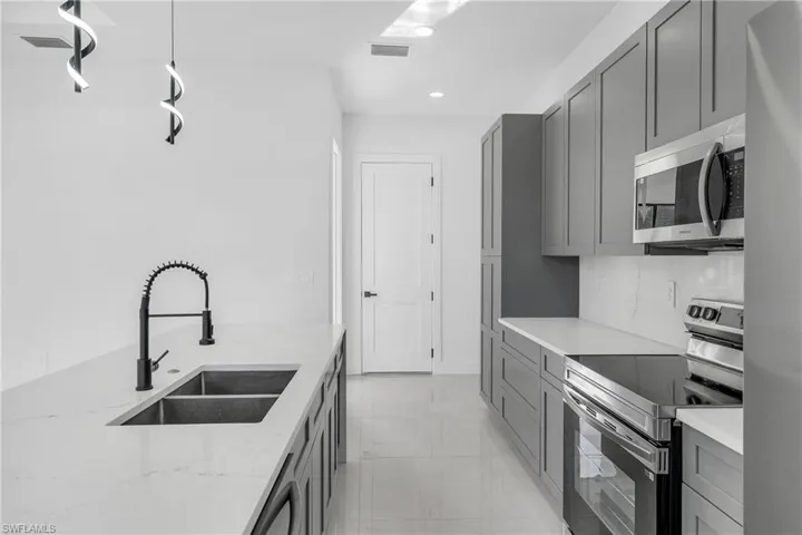 Kitchen with stainless steel appliances, gray cabinets, light stone countertops, recessed lighting, and decorative backsplash