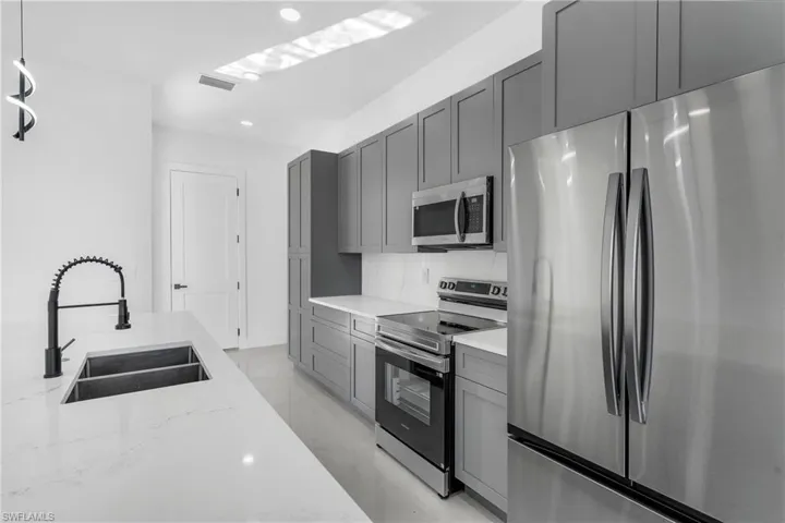 Kitchen with stainless steel appliances, gray cabinets, light stone counters, and recessed lighting
