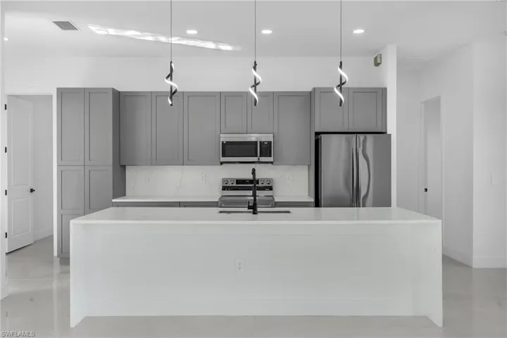 Kitchen featuring light stone countertops, stainless steel appliances, a kitchen island with sink, gray cabinetry, and hanging light fixtures