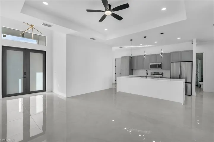 Unfurnished living room featuring a tray ceiling, ceiling fan, french doors, and recessed lighting